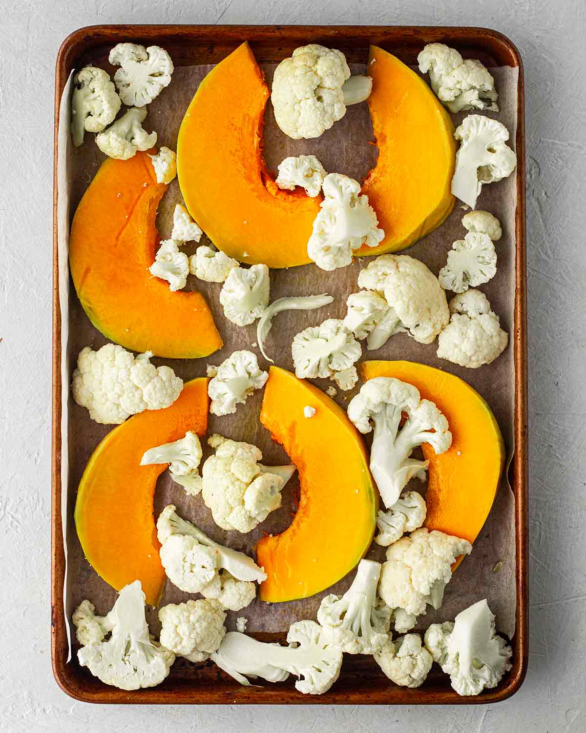 Lined baking tray with raw cauliflower and pumpkin