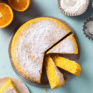 Simple vegan orange cake dusted with icing sugar on plate with a few slices coming out showing beautiful orange hue