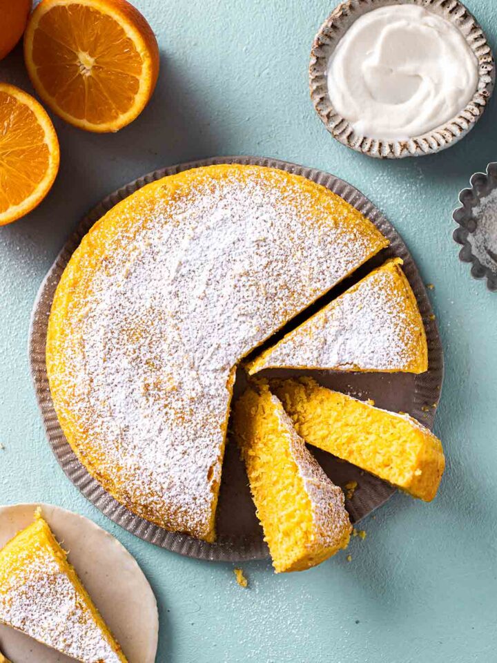 Simple vegan orange cake dusted with icing sugar on plate with a few slices coming out showing beautiful orange hue