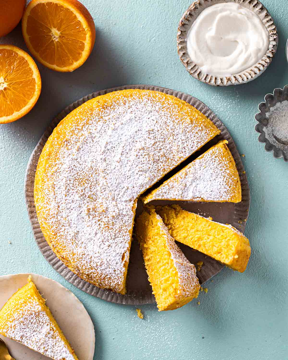 Simple vegan orange cake dusted with powdered sugar on plate with a few slices coming out showing beautiful orange hue.