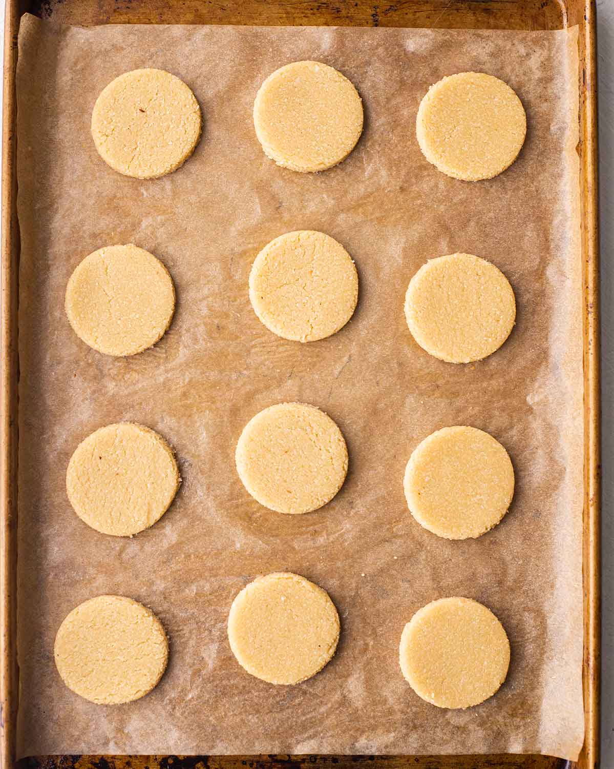 Lined baking tray of 12 unbaked round vegan gluten free shortbread.