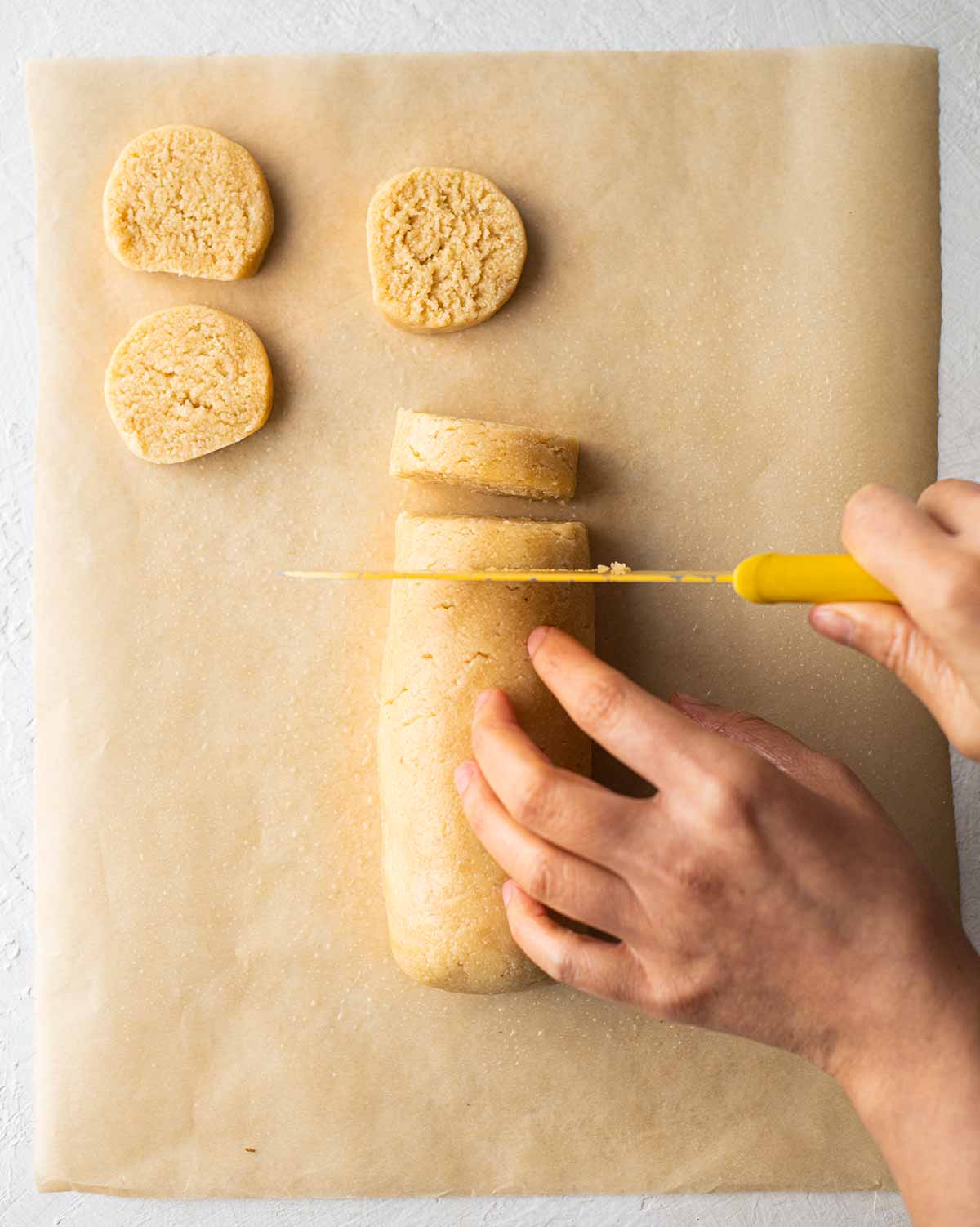 A tight log of cookie dough which is being sliced into round cookies.