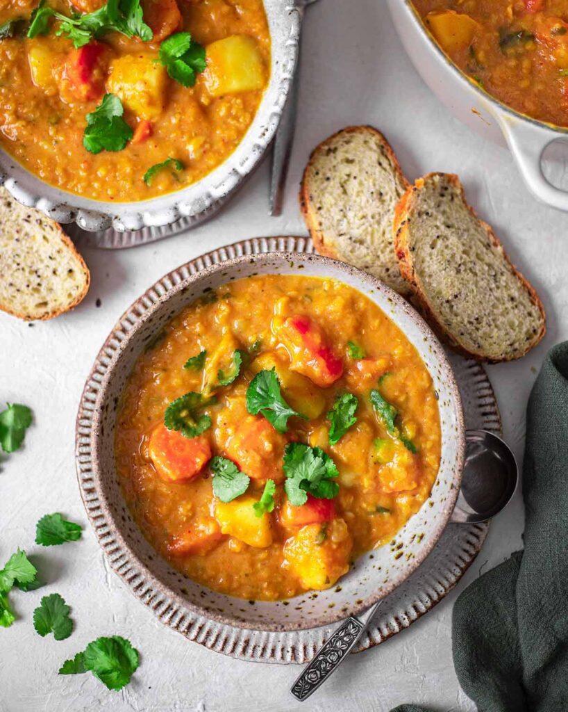 Thai red curry lentil soup in two bowls with a side of crusty bread.