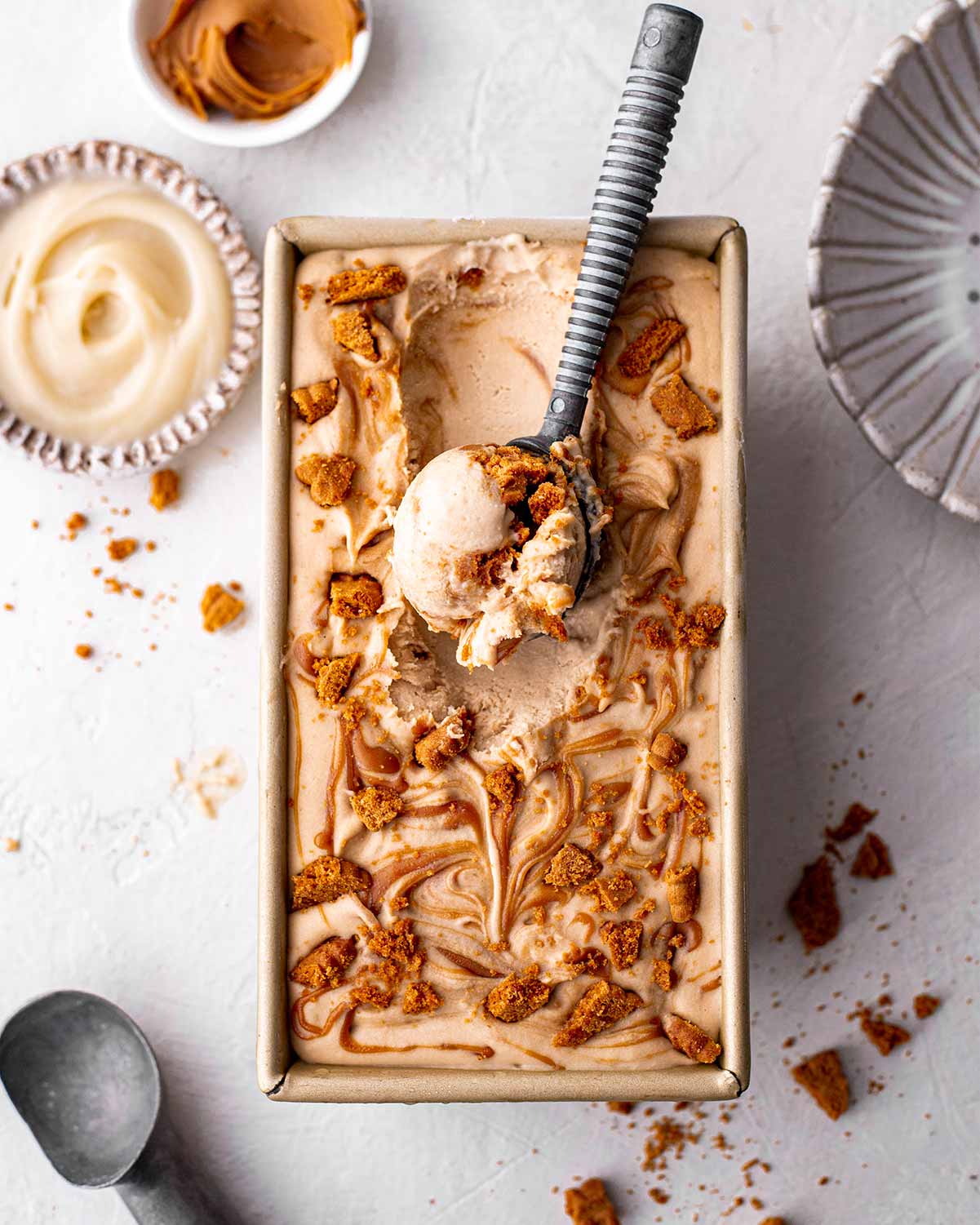 No churn vegan biscoff ice cream in a loaf pan with scoop of creamy ice cream coming out.