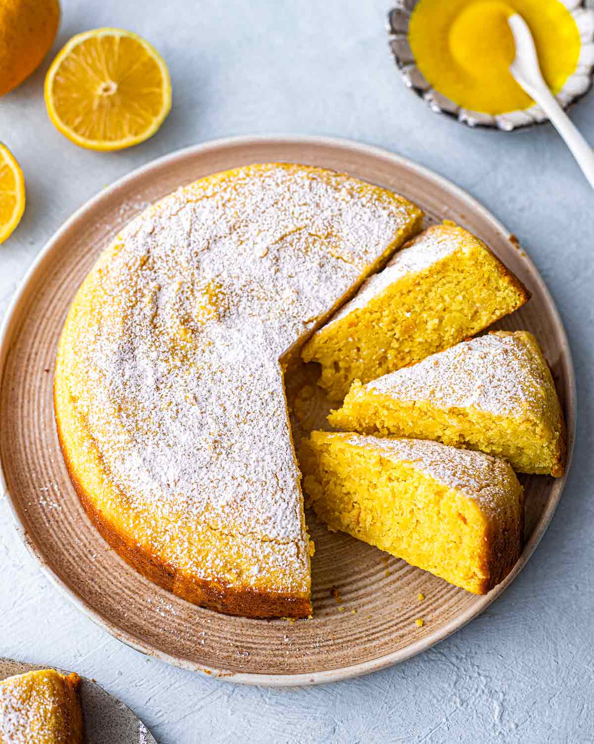 Whole vegan lemon cake on plate with slices coming out revealing bright yellow hue.