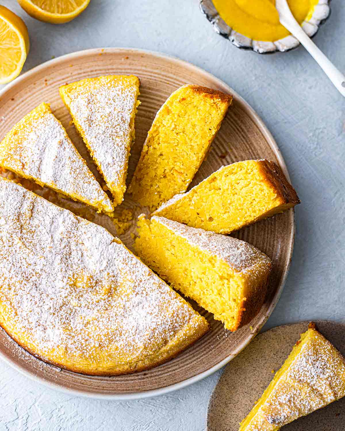 Top angle of whole vegan lemon cake on plate with slices coming out revealing bright yellow hue.