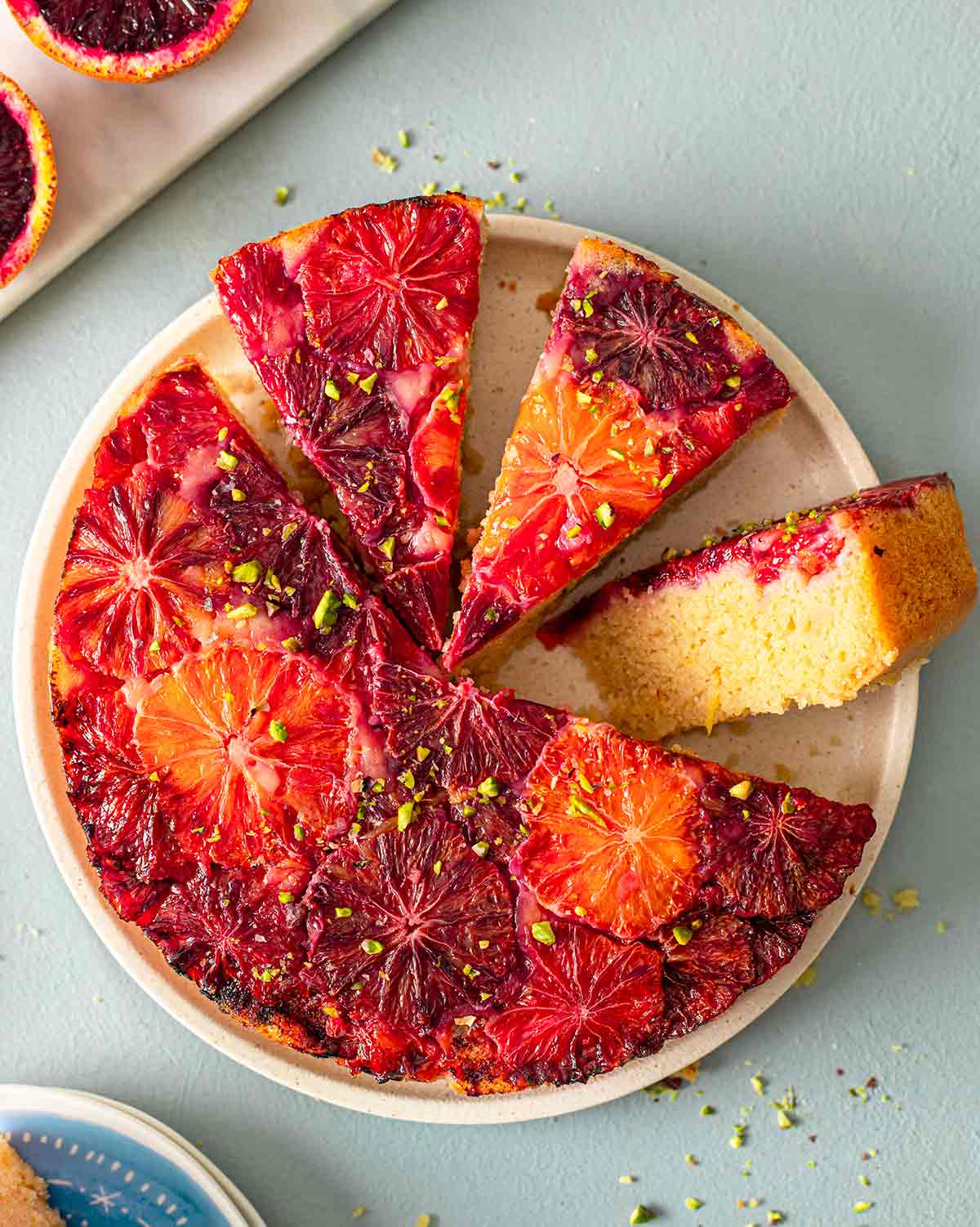 Upside down vegan blood orange cake on plate with a few slices cut out revealing golden fluffy interior.