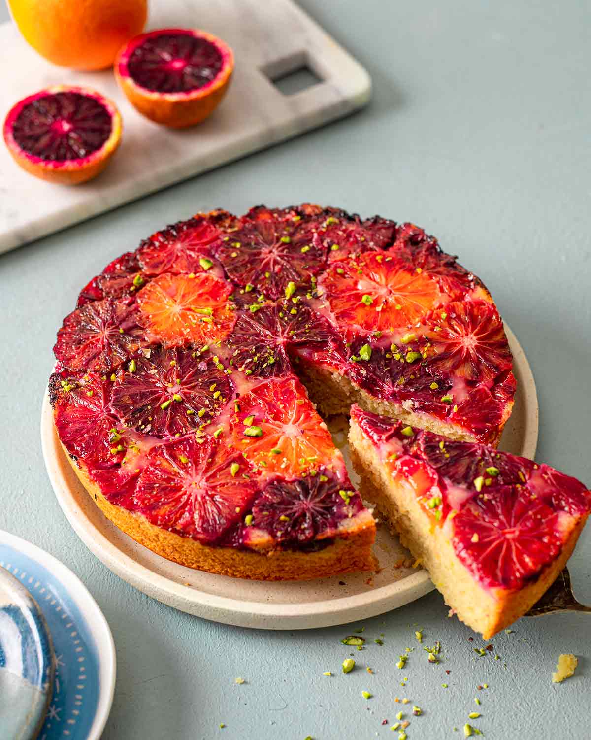 Cake on plate with one slice coming out focusing on orange and red hues of the blood oranges on top.