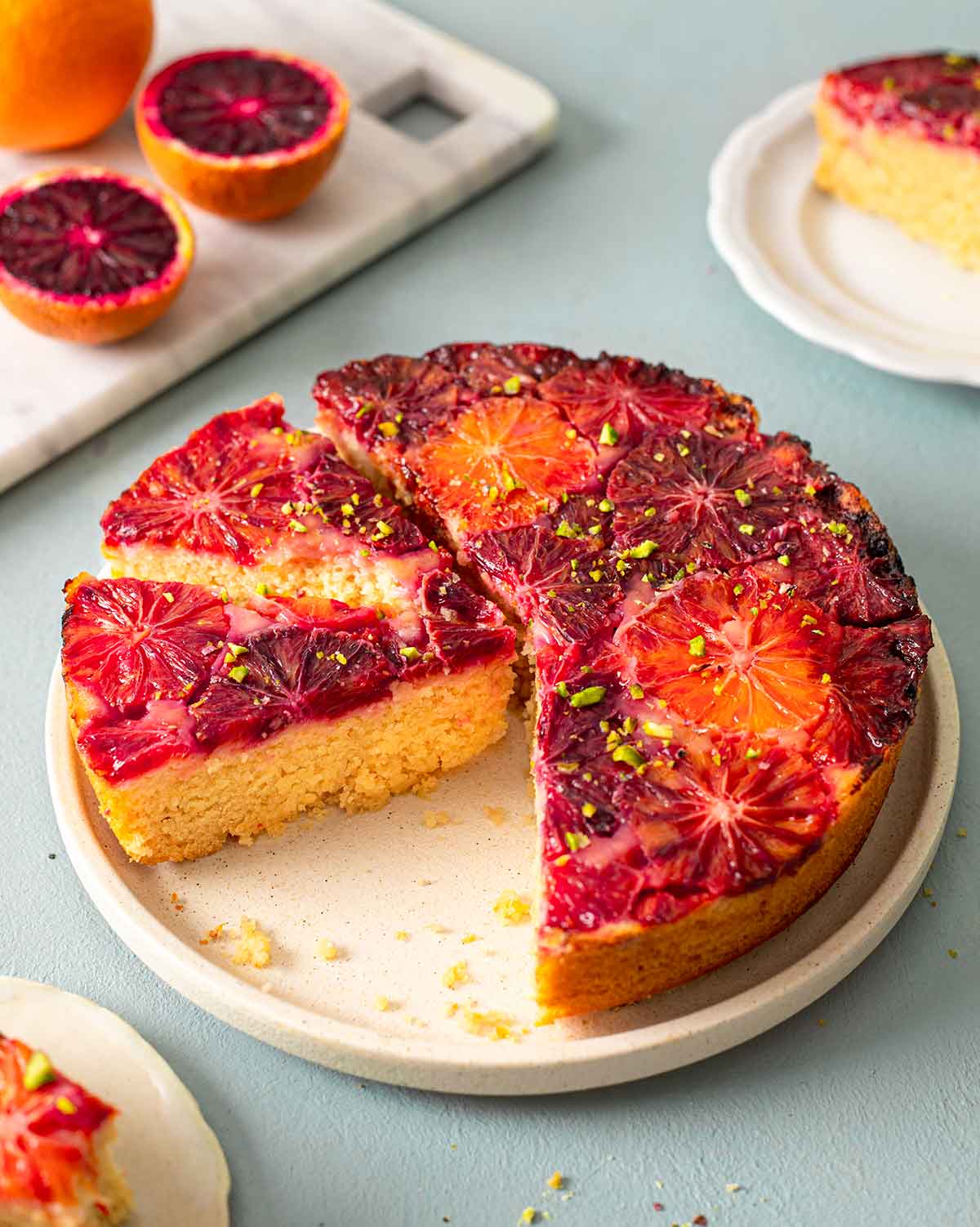 Blood orange cake on plate with a few slices cut out revealing fluffy golden cake.