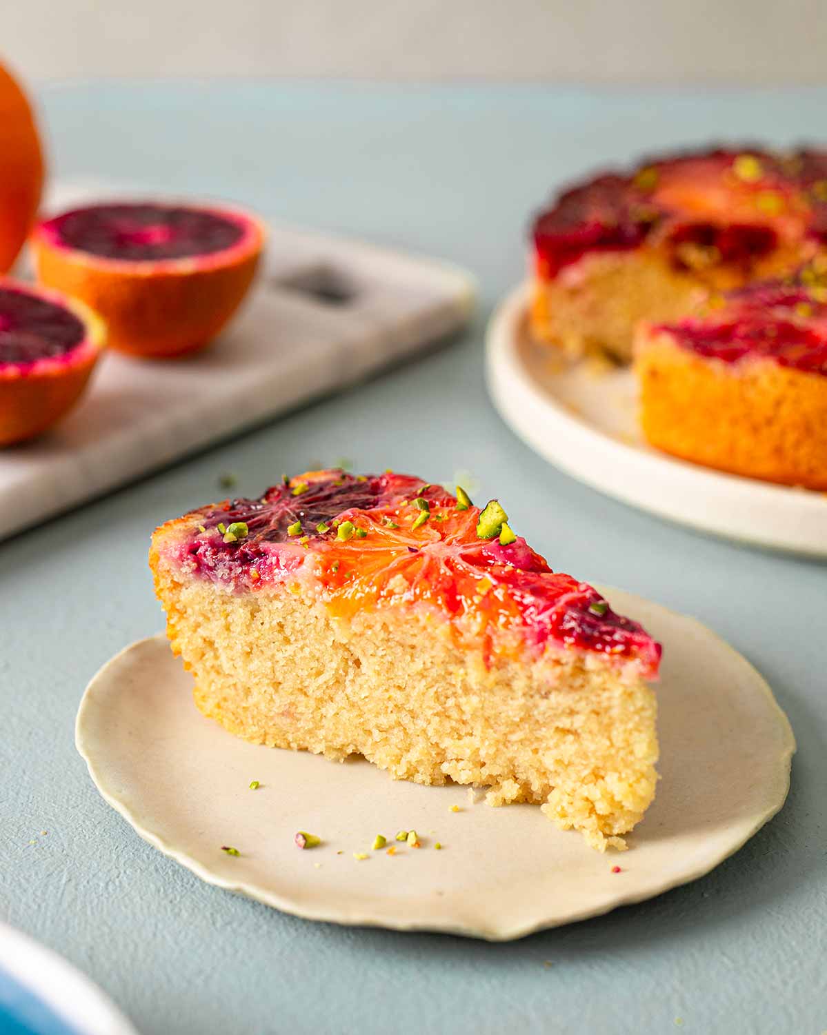 Close up of individual blood orange cake slice. The cake is golden and fluffy and has shiny blood orange slices on top.