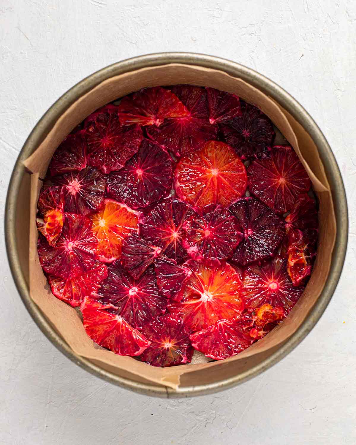 Overhead image of sliced blood oranges in bottom of lined cake pan.