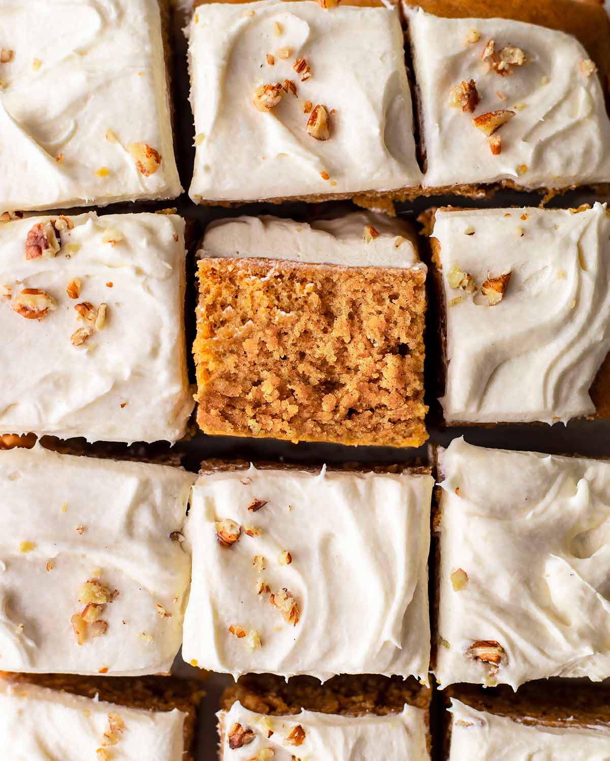 Close up of texture of individual square of sweet potato cake surrounded by frosting squares of the cake.
