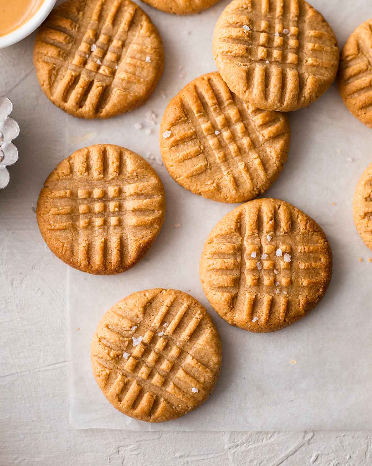 3 ingredient vegan peanut butter cookies with criss cross pattern and flaked salt on baking paper.