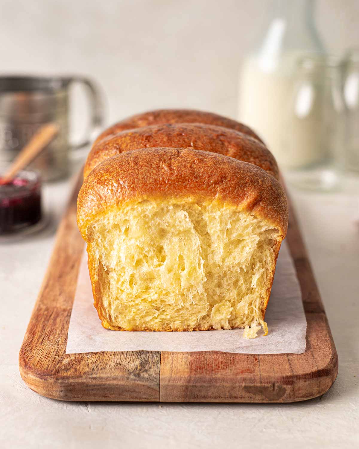 Vegan brioche on chopping board with slice torn off revealing soft and fluffy interior.