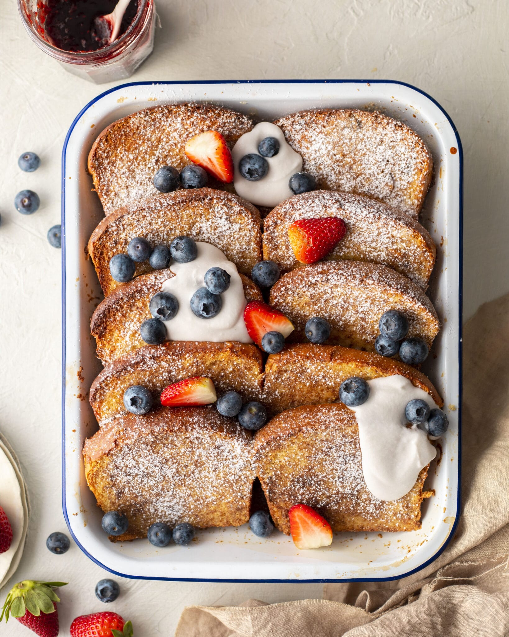 Baked vegan french toast where vegan brioche is cut into slices. The french toast are dusted with sugar and have cream and berries on top.