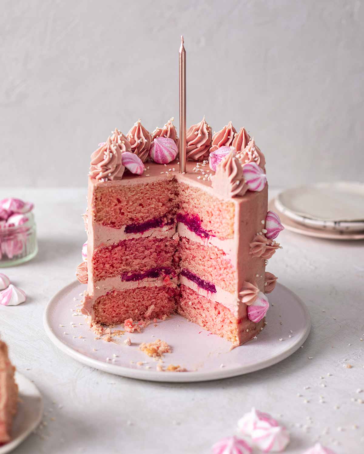 Cross section of cake revealing fluffy pink cake, layers of strawberry jam and baby pink buttercream.