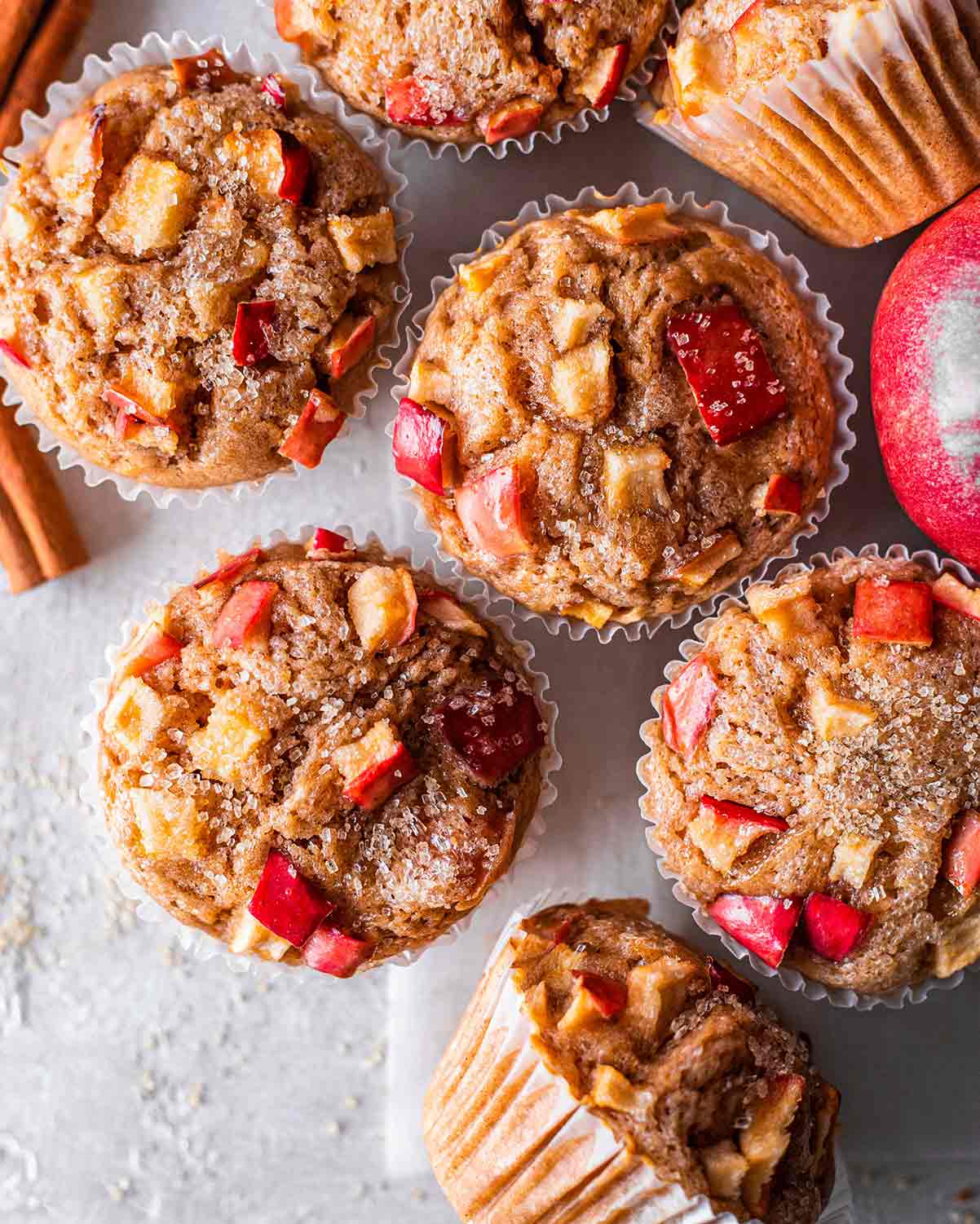 Flatlaye of apple muffins showing golden muffins tops, especially red apple chunks and granulated sugar.