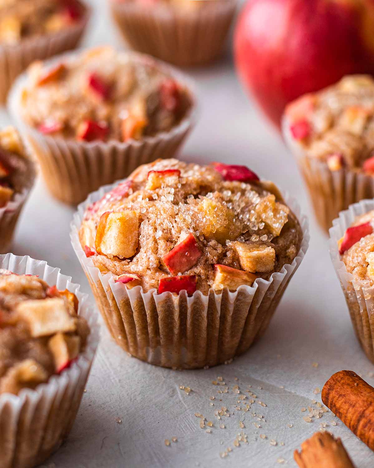 Vegan apple muffins with chunks of red apple and raw granulated sugar baked into the top of each muffin.