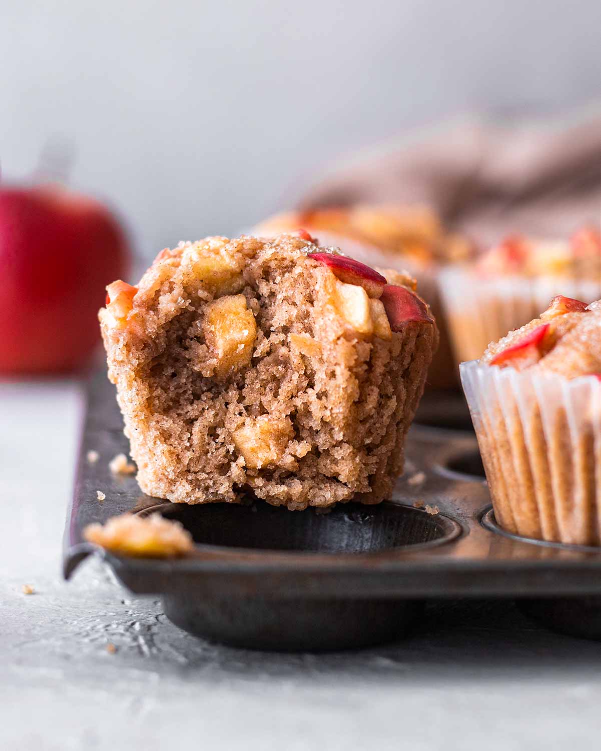 Close up of one apple muffin with bite taken out showing fluffy texture and apple chunks.