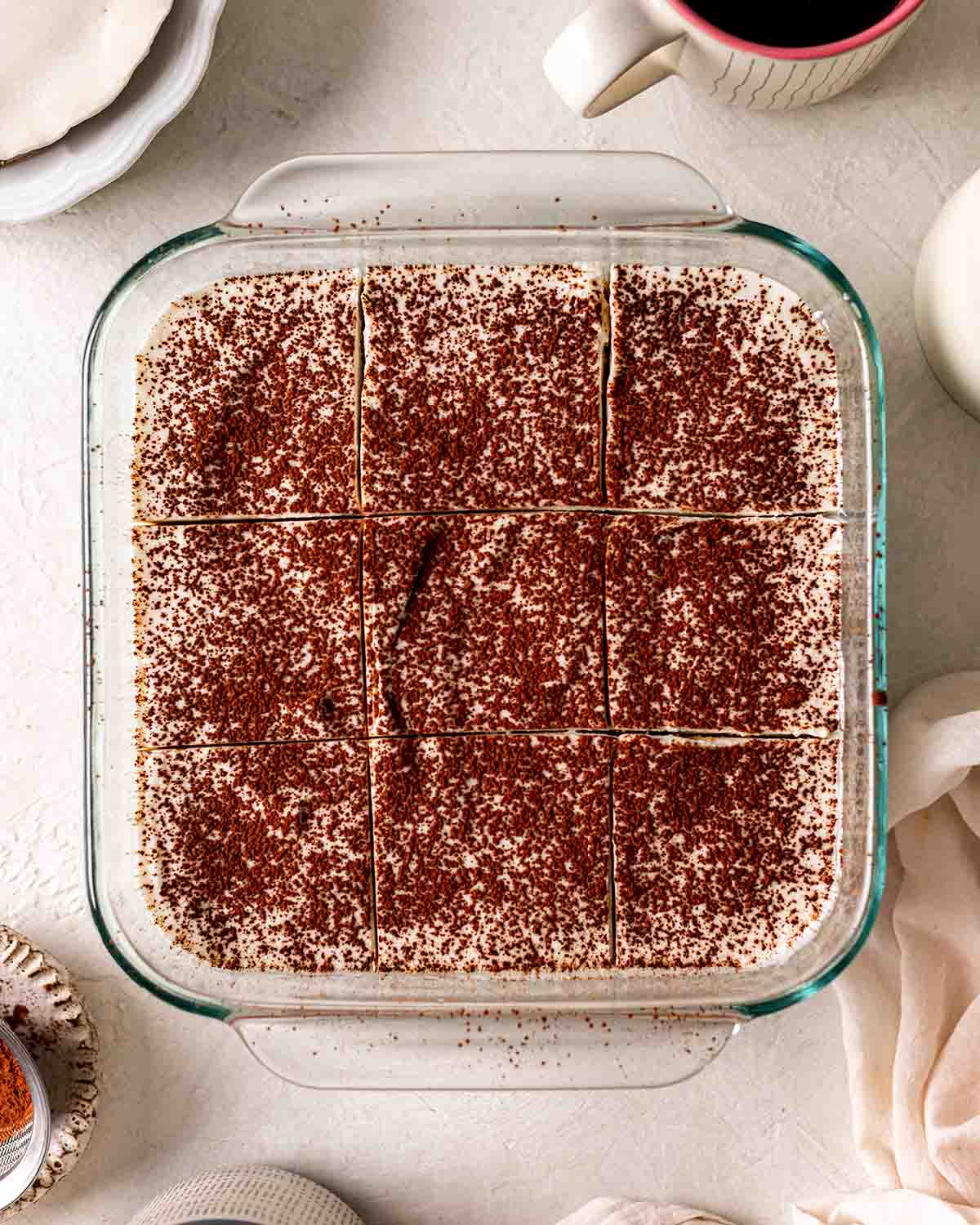 Overhead image of tiramisu cut up in baking tray with a light dusting of cocoa.