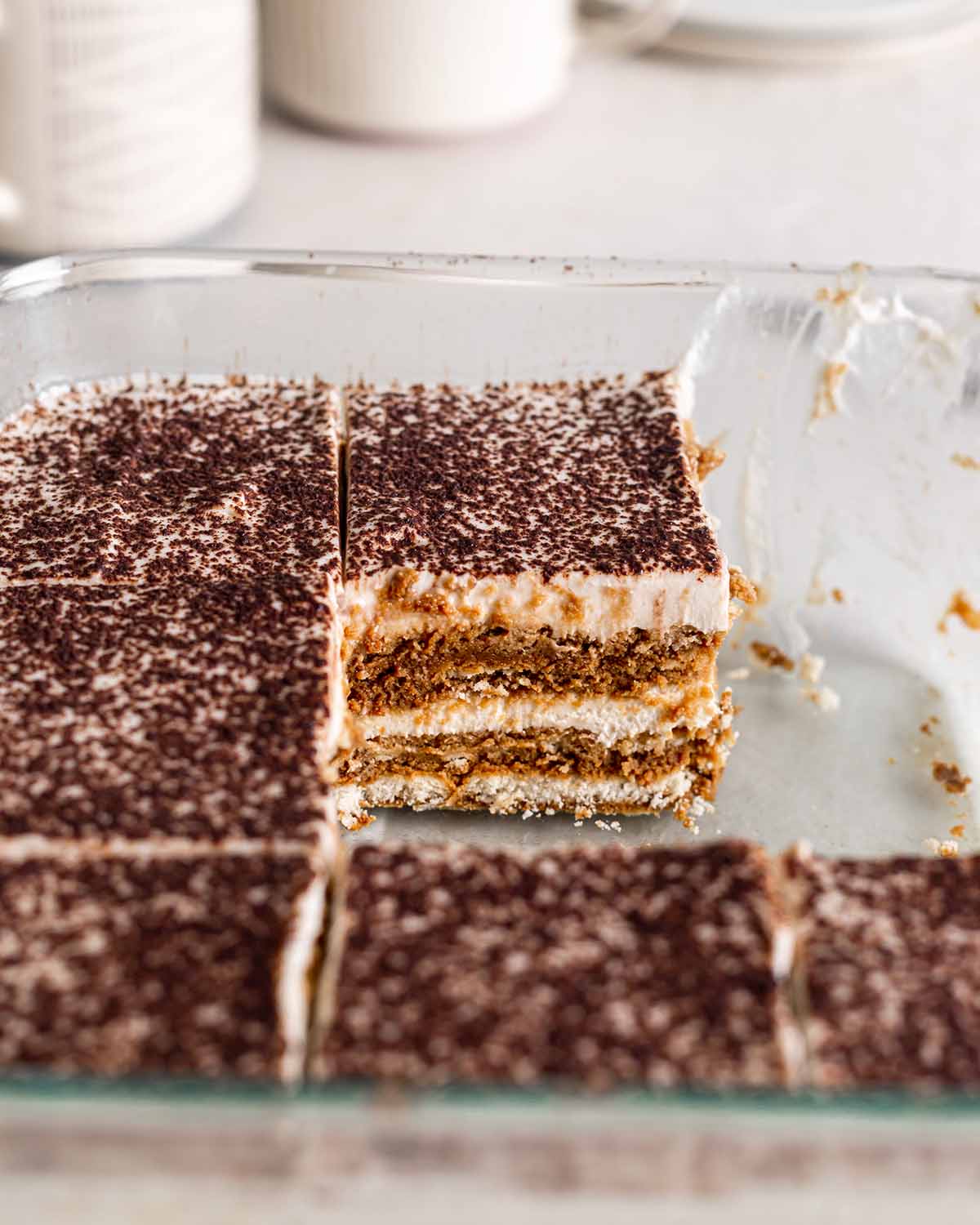 Slices of tiramisu in glass baking dish with close up of one slice revealing straight layers.