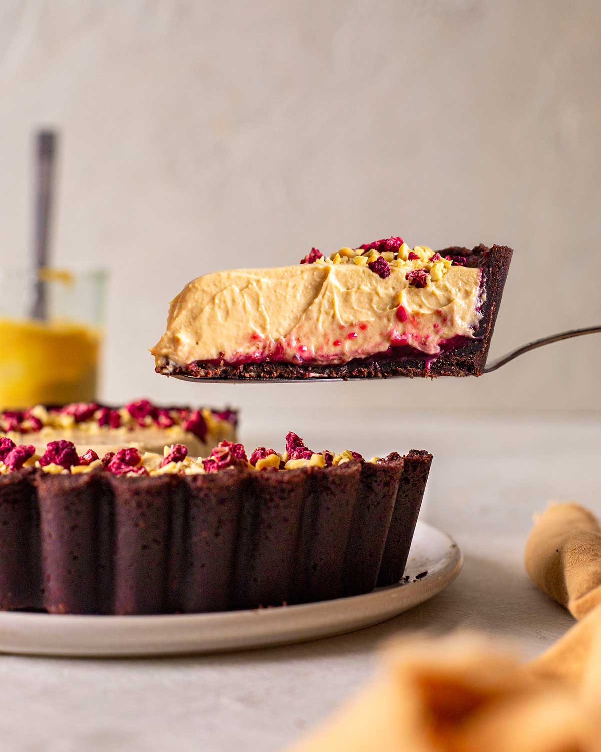 Slice of pie lifted in air revealing soft mousse, bright raspberry jam and dense chocolate crust.