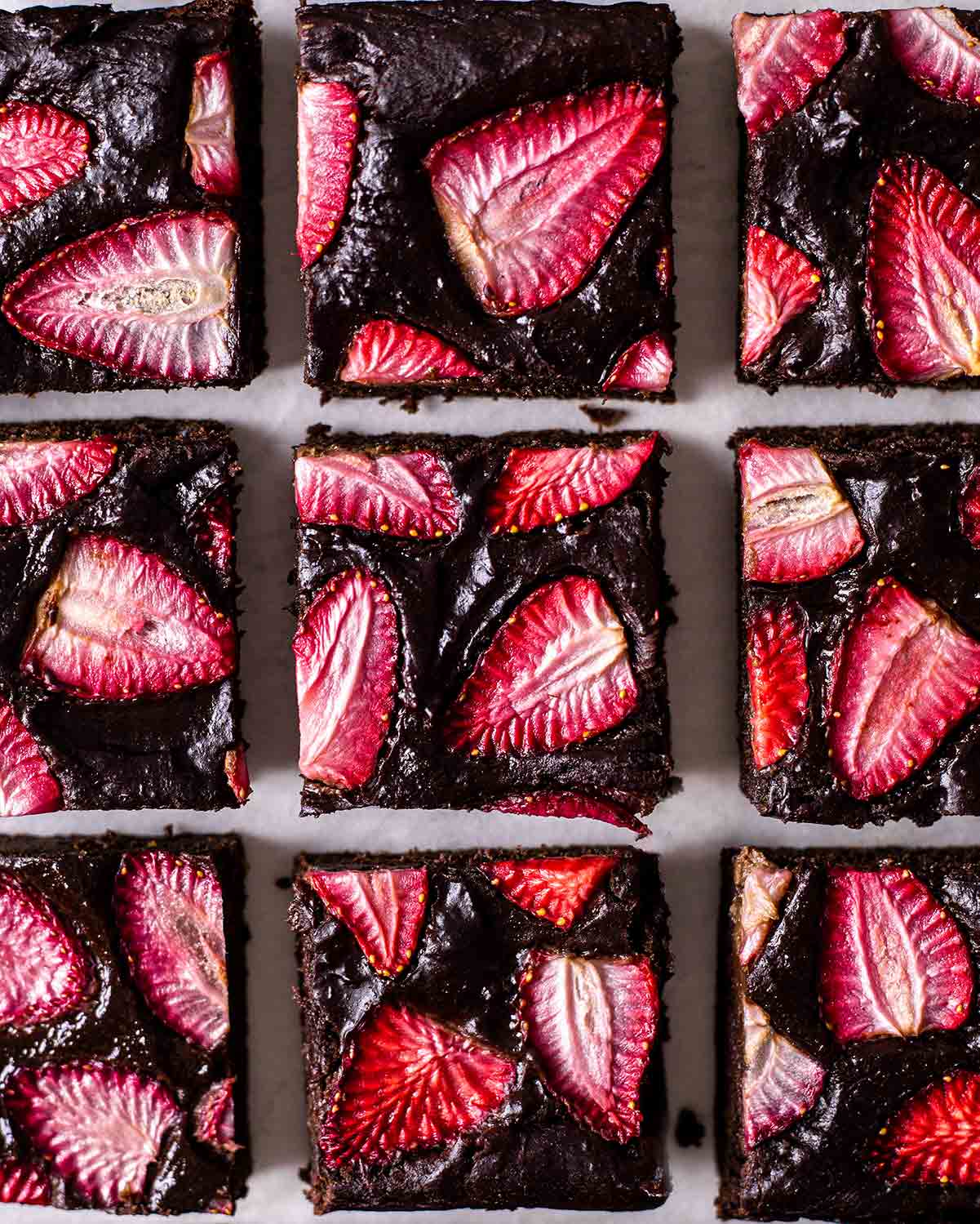 Flatlay of sliced protein brownies with a shiny surface and sliced strawberries throughout.