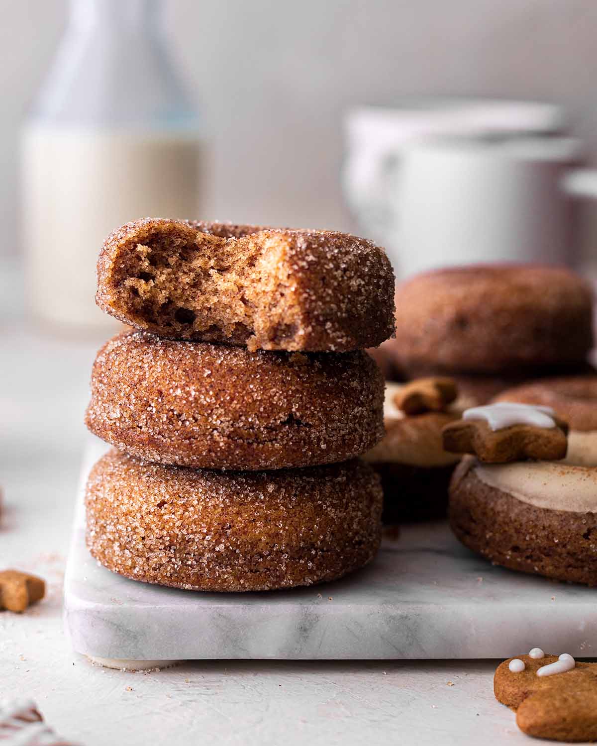 Stack of gingerbread donuts covered in cinnamon sugar. Top donut has a bite taken out showing fluffy texture.