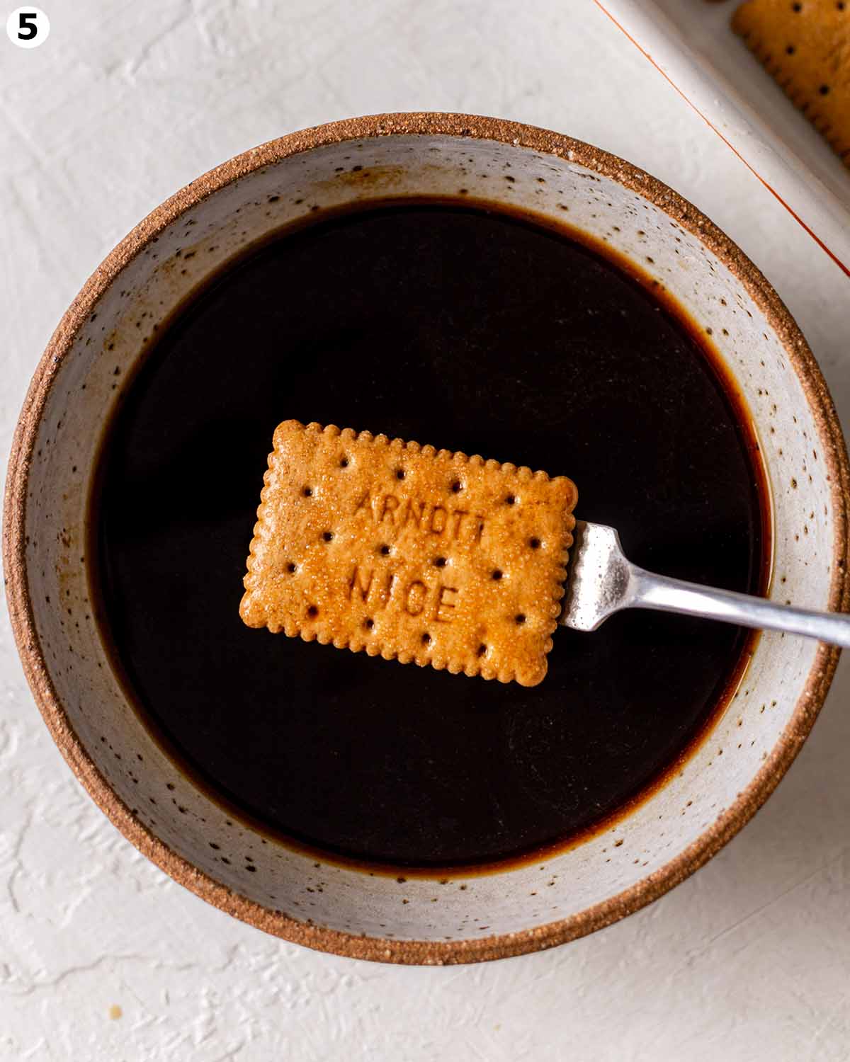 Close up of cookie on fork after it's been dipped in black coffee.