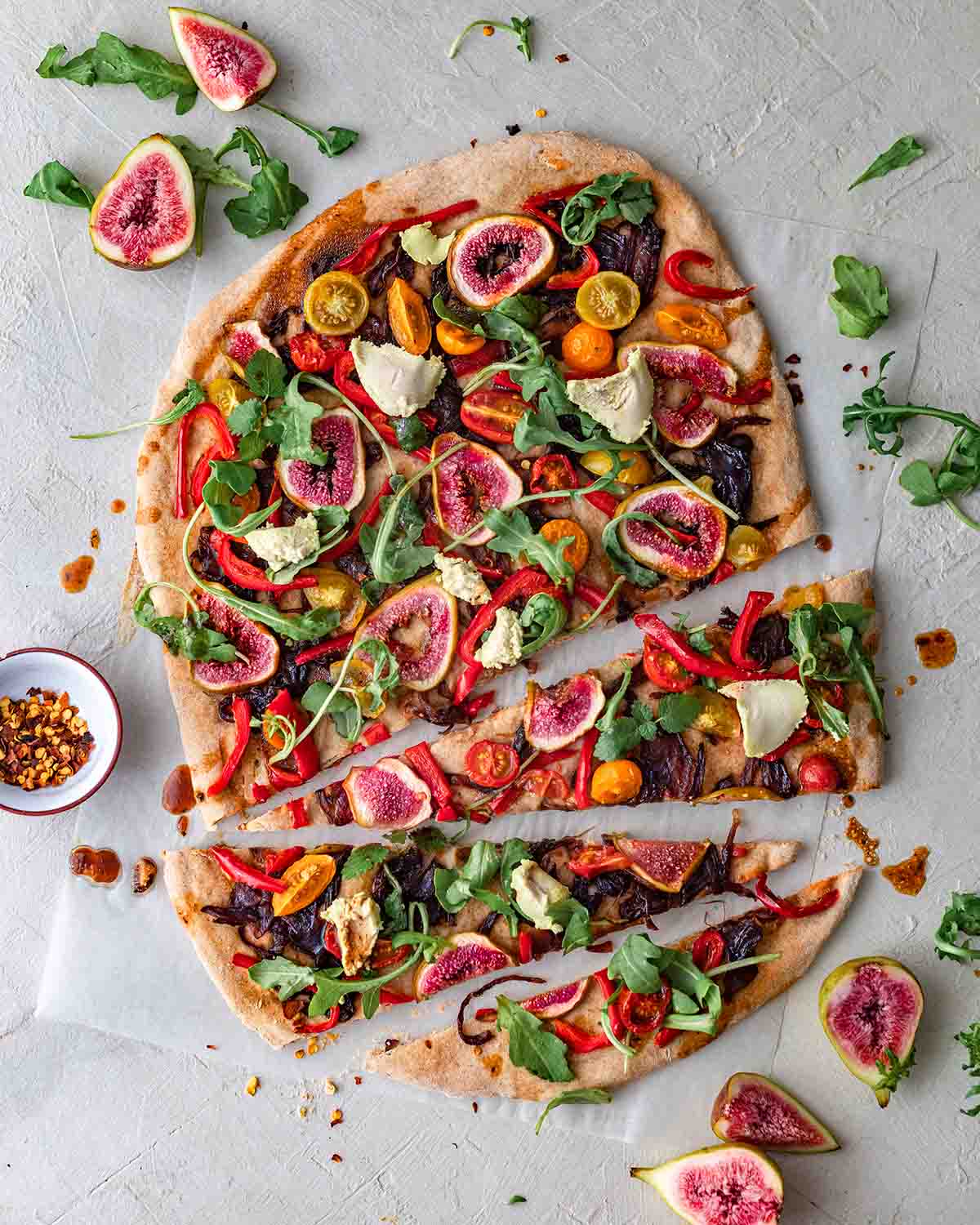 Large fig and caramelized onion pizza with bright toppings on sheet of baking paper. Three slices are cut out of pizza.