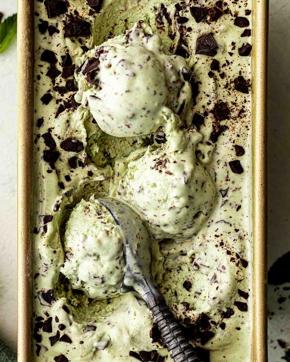 Close up of melting mint chocolate chip ice cream in loaf tin.