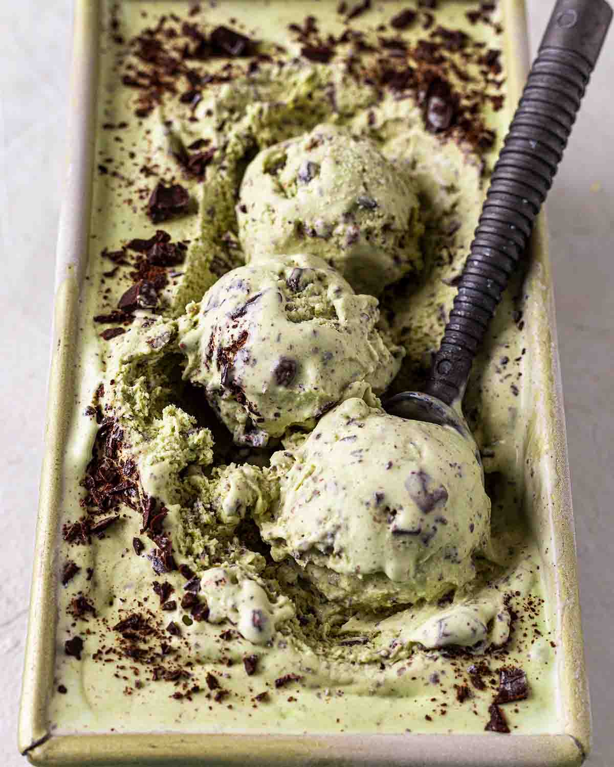 Side close up of melting mint chocolate chip ice cream in loaf tin.