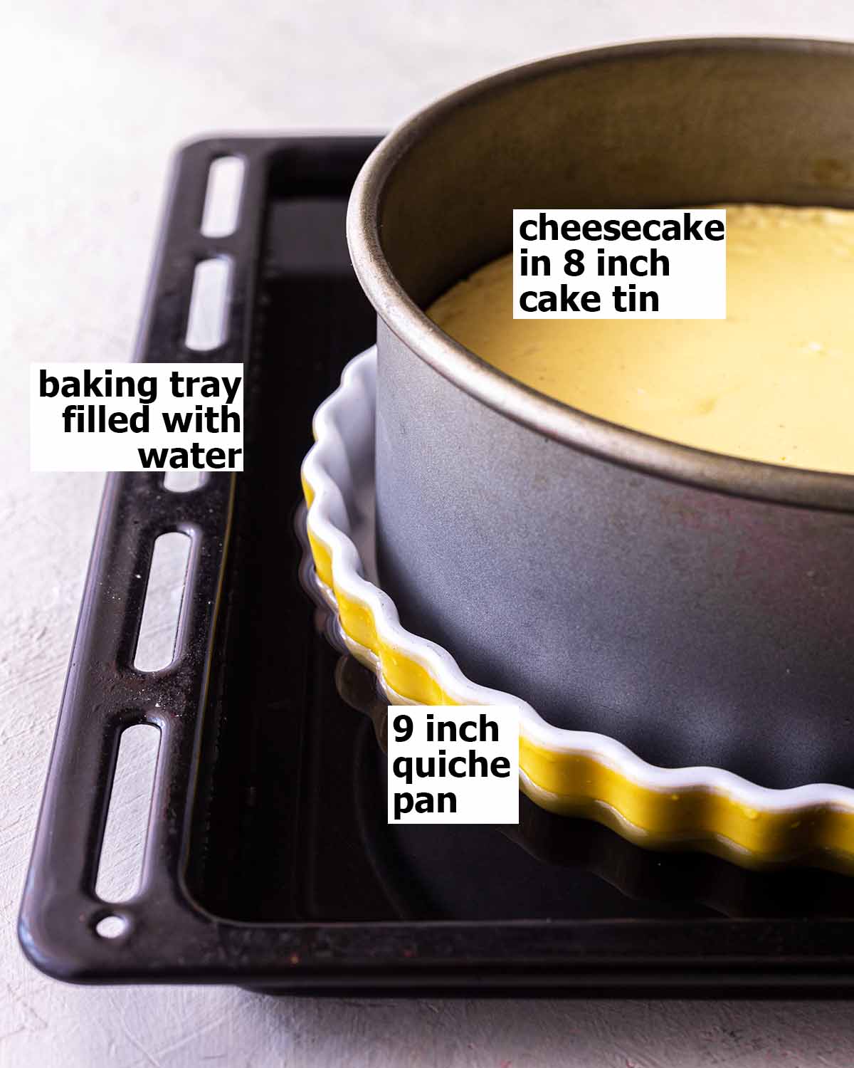 Cheesecake in cake tin sitting in larger quiche pan sitting in a large baking tray filled with water.