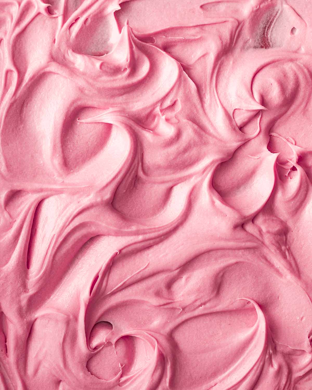 Close up of pink strawberry frosting with lots of swirls showing soft creamy texture.
