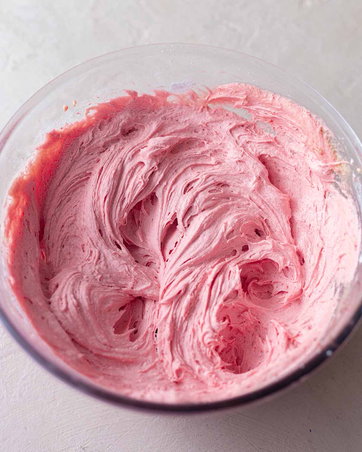 Bowl of whipped and fluffy pink-coloured strawberry cream cheese frosting.