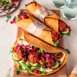 Maple BBQ cauliflower wraps on chopping board. One wrap is only half closed revealing saucy cauliflower.