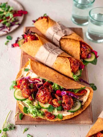 Maple BBQ cauliflower wraps on chopping board. One wrap is only half closed revealing saucy cauliflower.