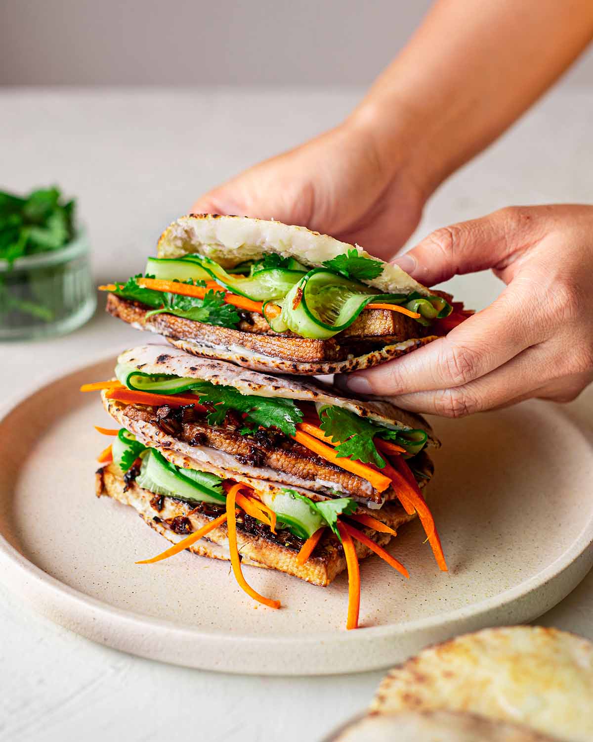 Hands holding pita wraps filled with tofu, vegetables and mayonnaise.