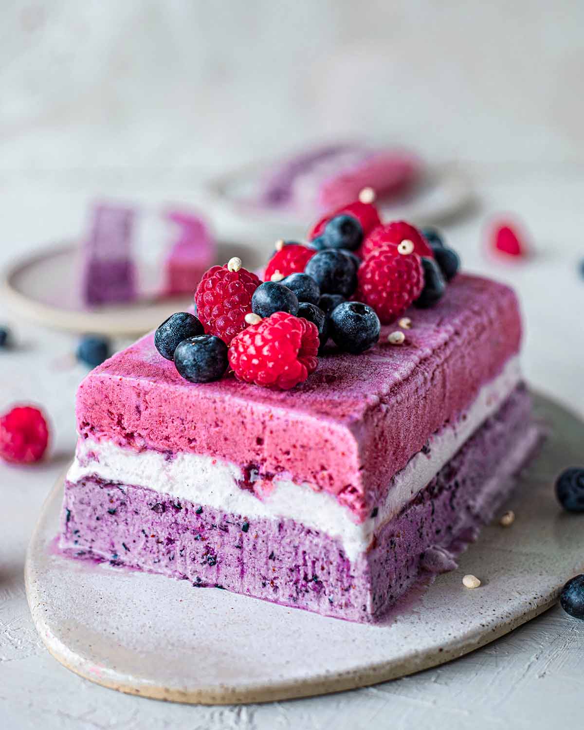 Vegan ice cream cake with blueberry, vanilla and raspberry layers topped with fresh berries