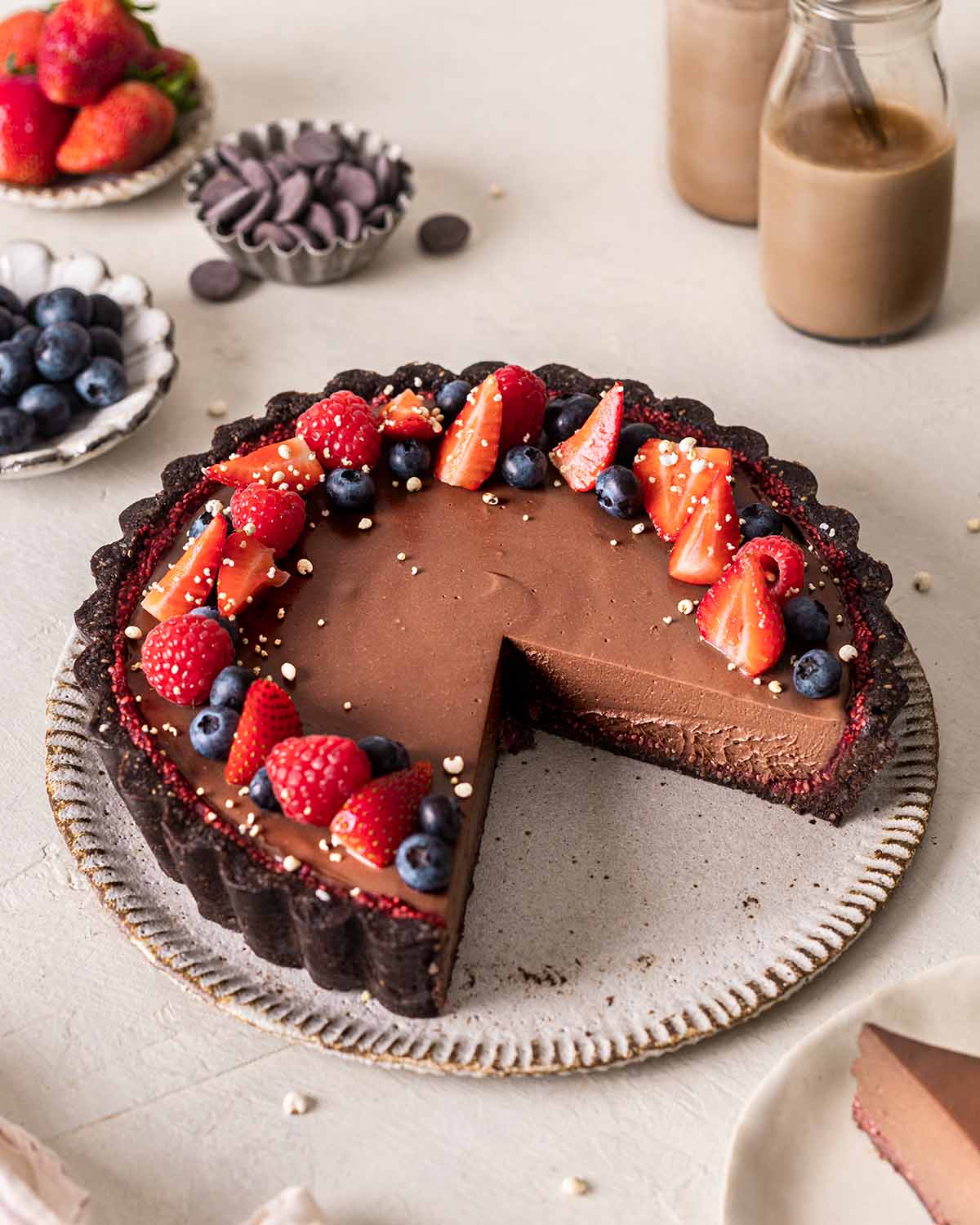 Vegan chocolate tart with berries on outer rim. Slices cut out of tart showing mousse-like texture.