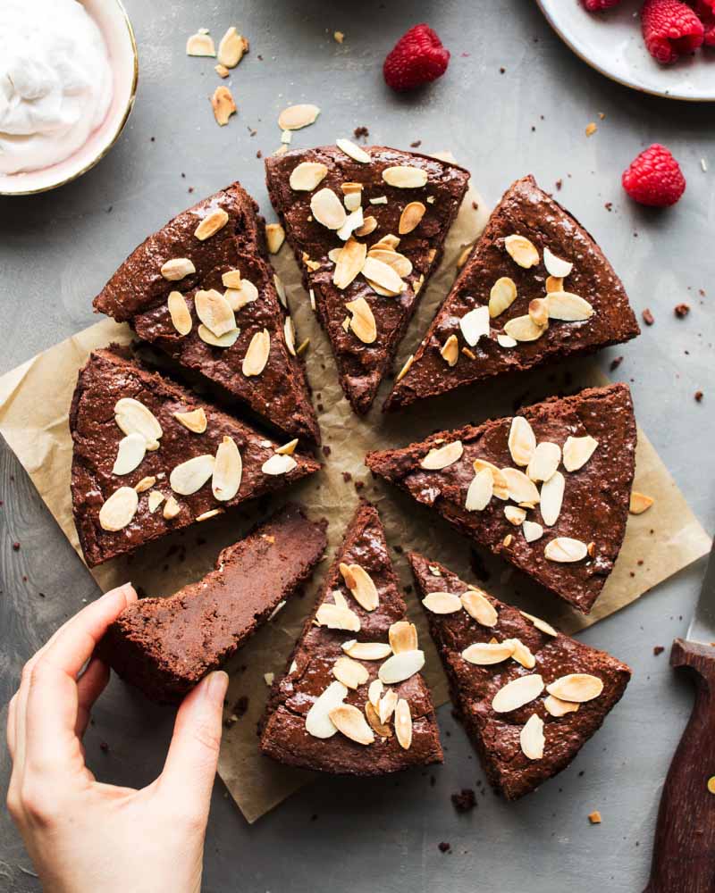 Overhead image of sliced fudgy chocolate cake with flaked almonds on top.