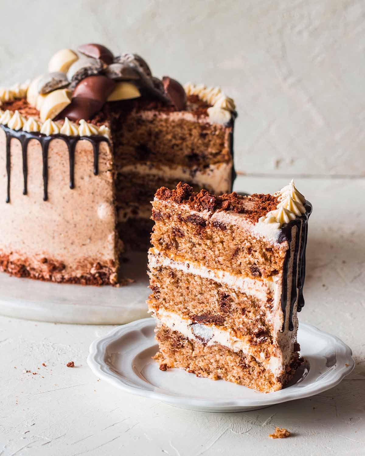 Close up of one slice of vegan oreo cake or cookie and cream cake. The slice has three layers of vanilla sponge packed with chocolate oreo cookies, a buttercream with bits of cookies and crushed cookies on top