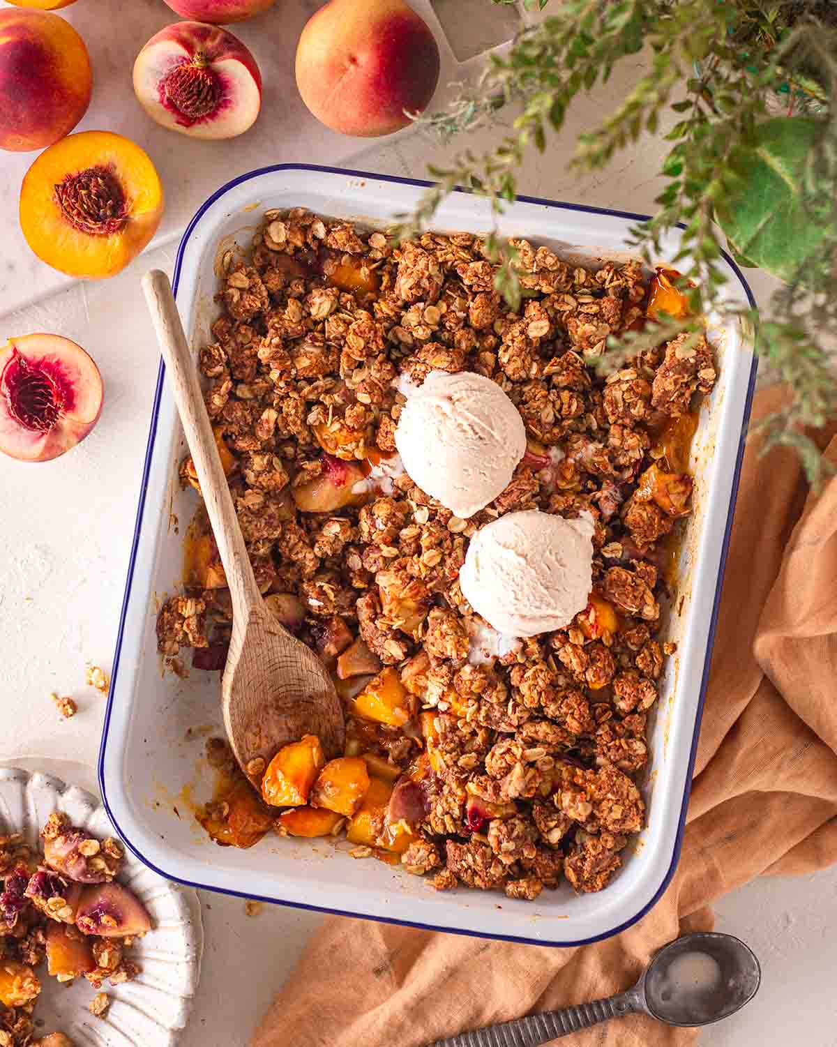 Vegan peach crisp in baking tray with wooden spoon coming out.