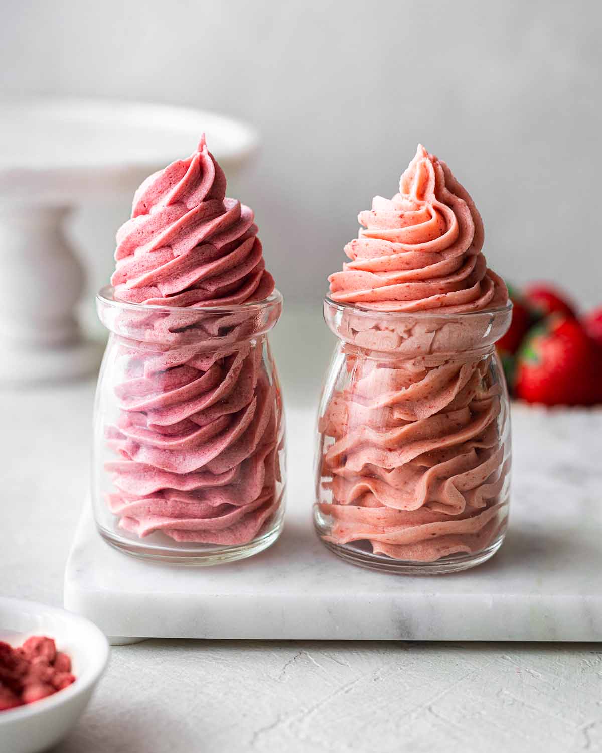 Two glass jars filled with the two versions of strawberry buttercream frosting.