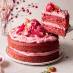 Vegan strawberry cake on plate with slice of cake lifted out revealing fluffy pink texture.