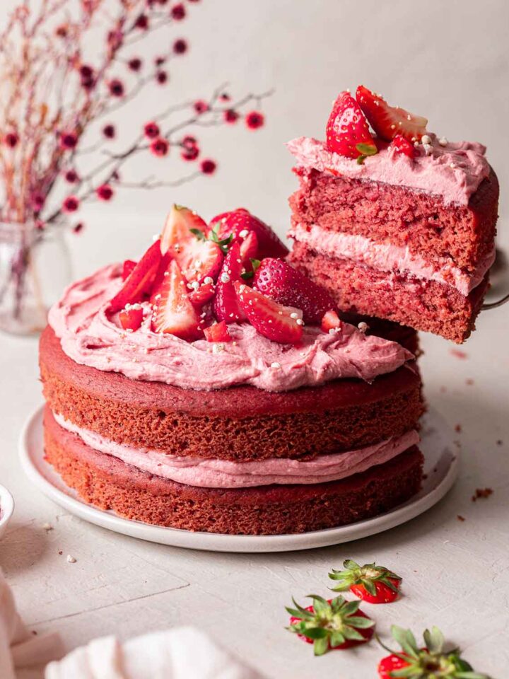 Vegan strawberry cake on plate with slice of cake lifted out revealing fluffy pink texture.