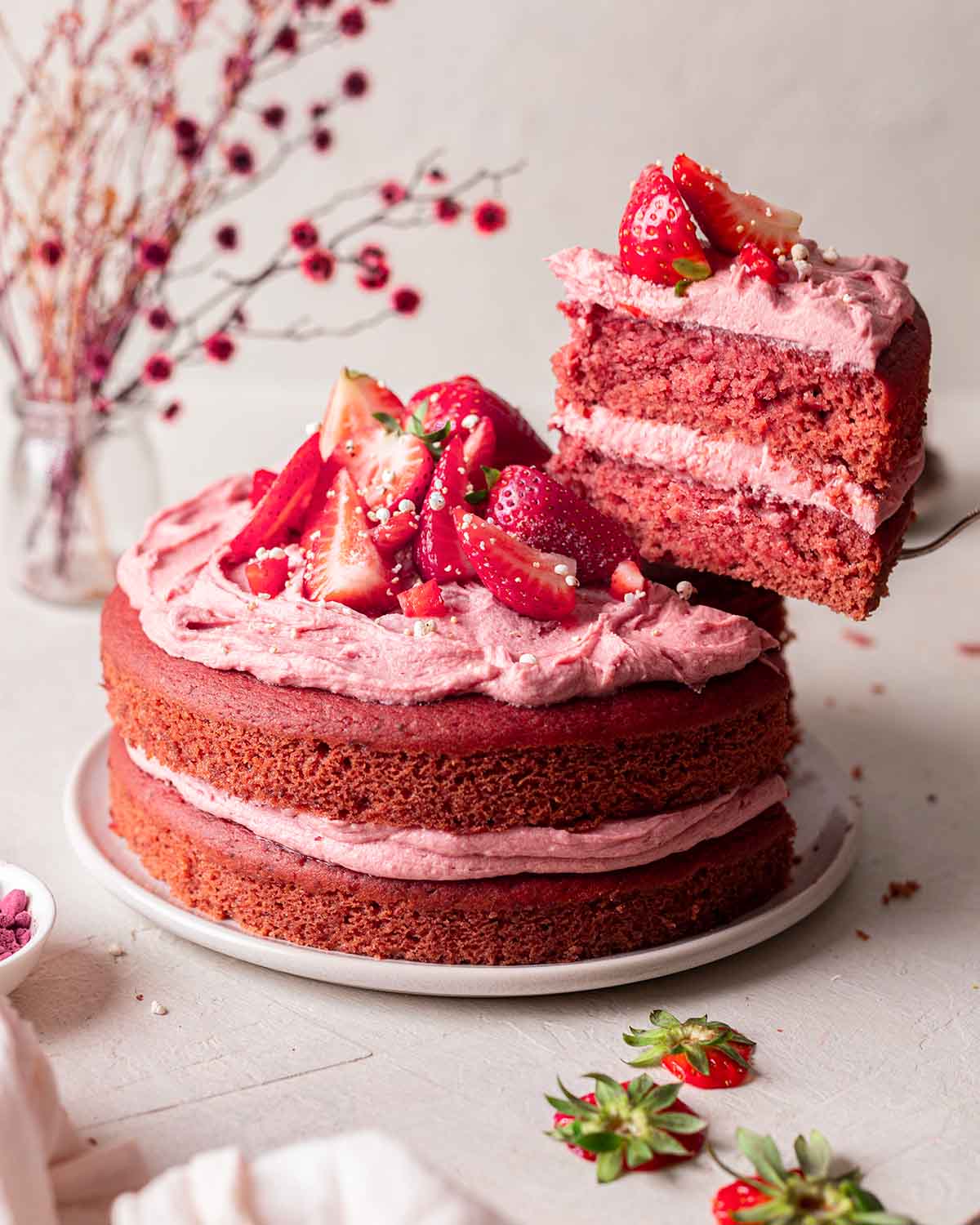 Vegan strawberry cake on plate with slice of cake lifted out revealing fluffy pink texture.