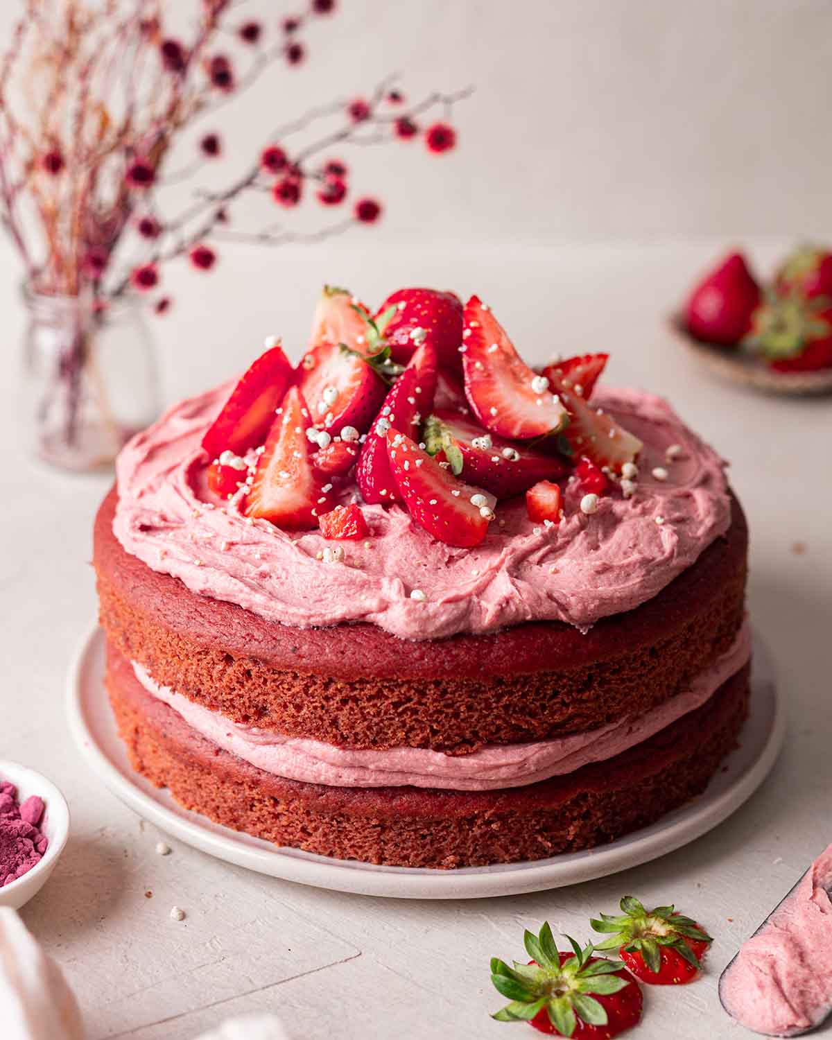 Two layer strawberry cake on plate decorated with pink frosting and fresh strawberries.