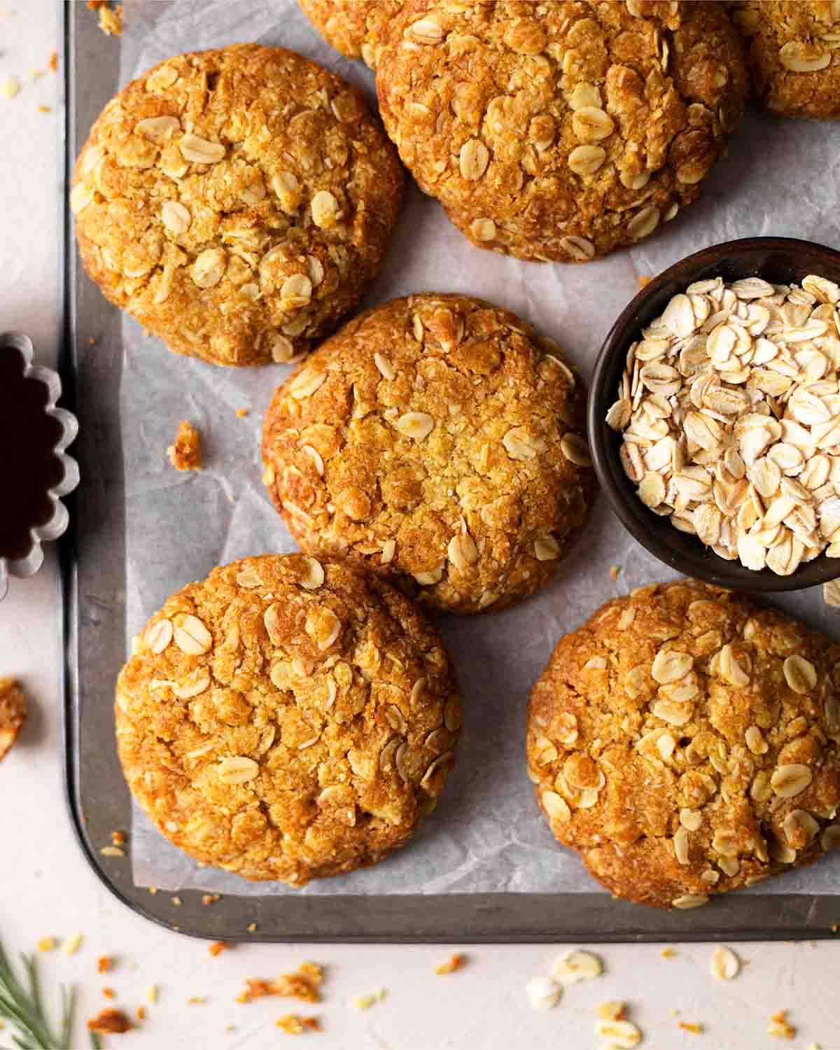 Flatlay of Anzac biscuits on baking tray with oats and golden syrup in background