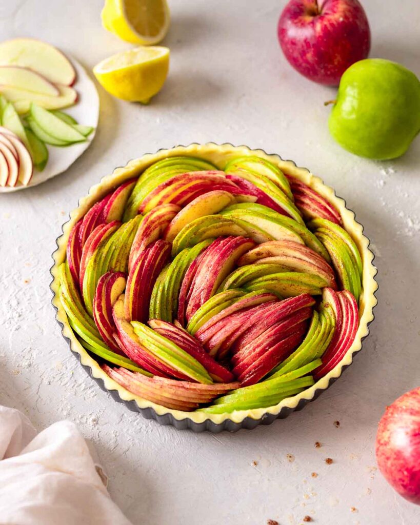 Unbaked vegan apple tart with lots of thinly sliced red and green apples.
